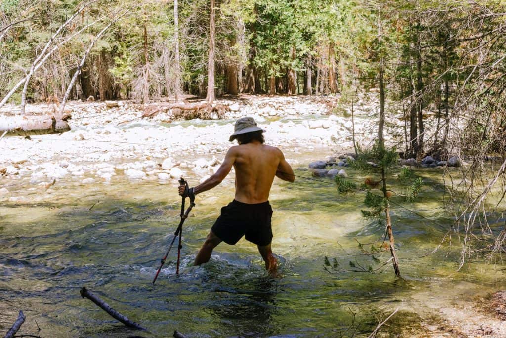 Shirtless man tries to cross a knee-high river