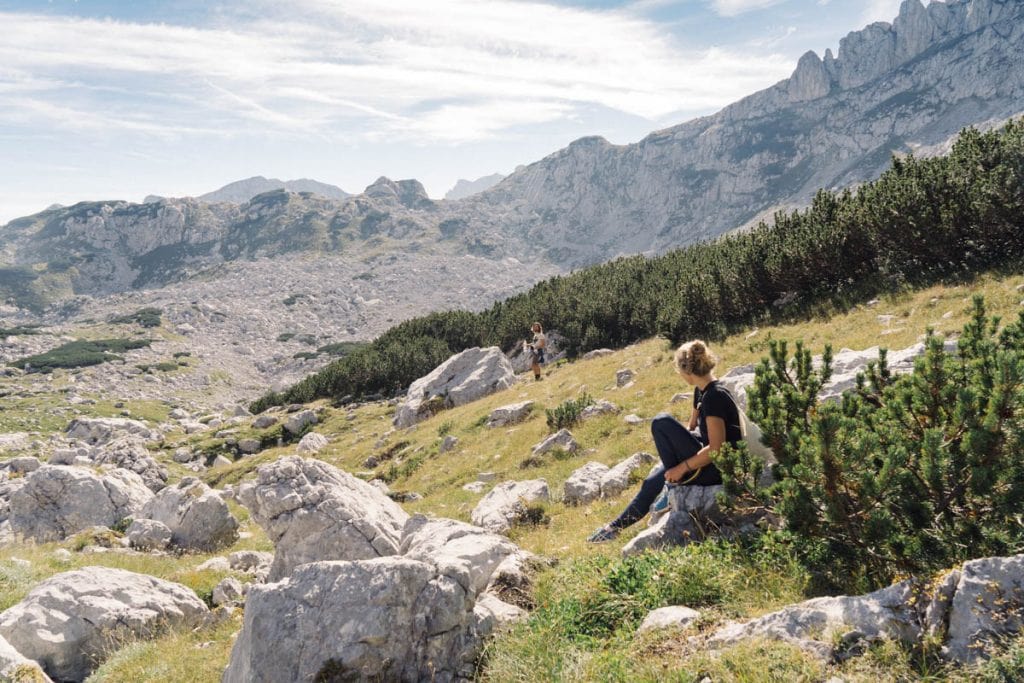 Person sits on grassy path with boulders to Bobotov Kuk