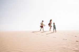 Family of three carry a sandboard as they walk on the sand dunes