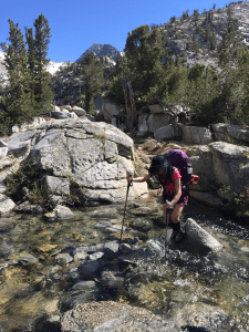 Hiker crossing river in Rae Lakes Loop with hiking poles