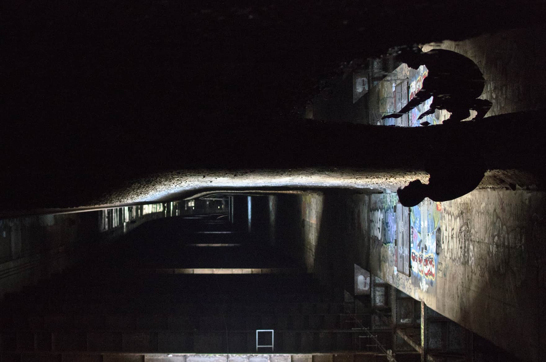 Crouching man is reflected in a puddle in the Freedom Tunnels of New York