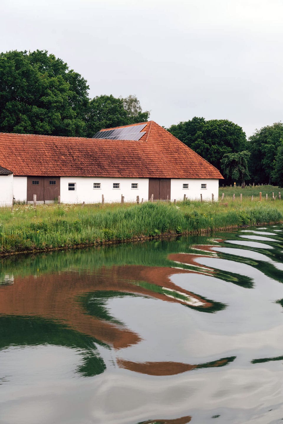 An old villa outfitted with solar panels is viewed from the canal where the boat's motion creates undulating waves