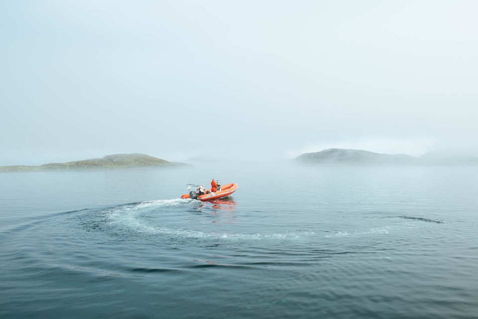 Man in a orange boat whips around in the misty sea