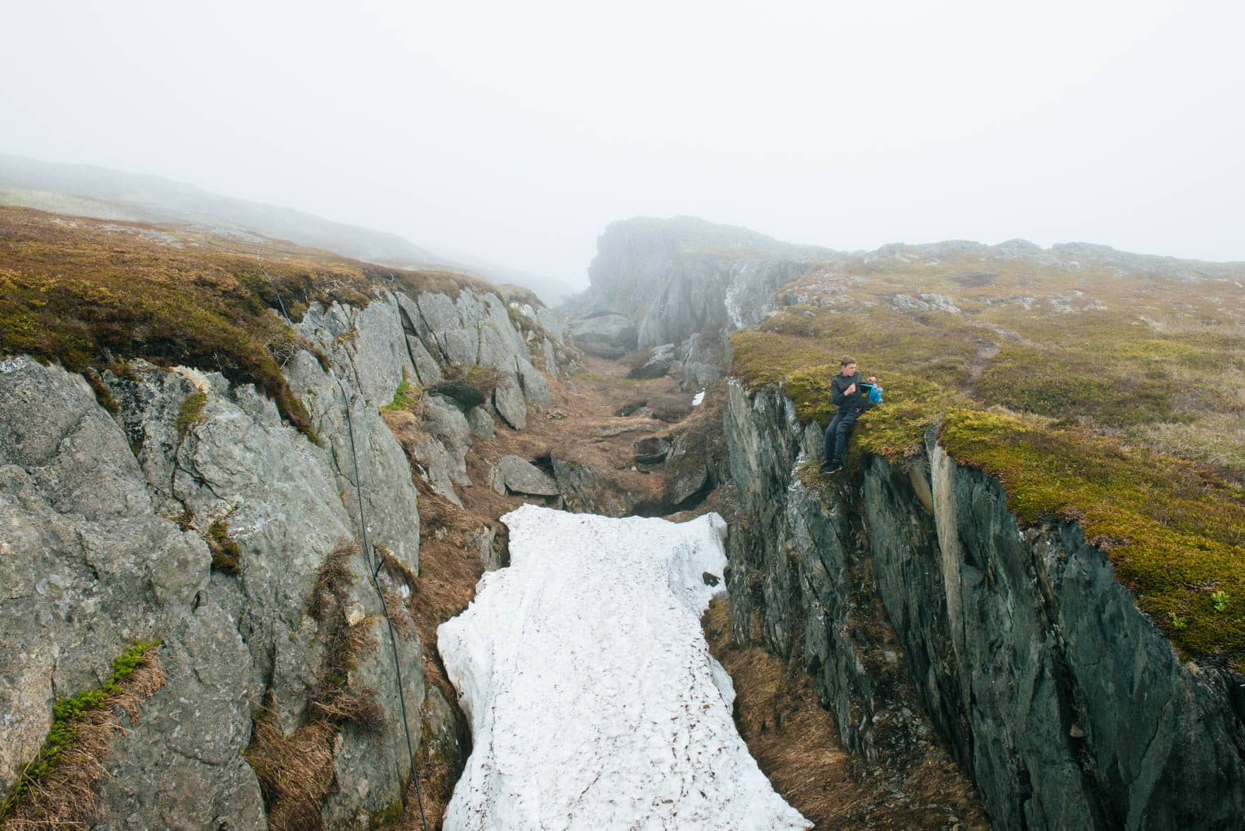 Child sits between a geological fault in a mossy Newfoundland landscape