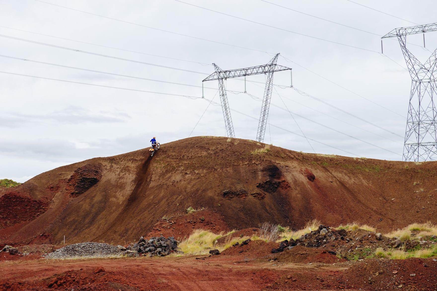 Solo Dirt bike cyclist rides up a tall red canyon with powerlines in the background