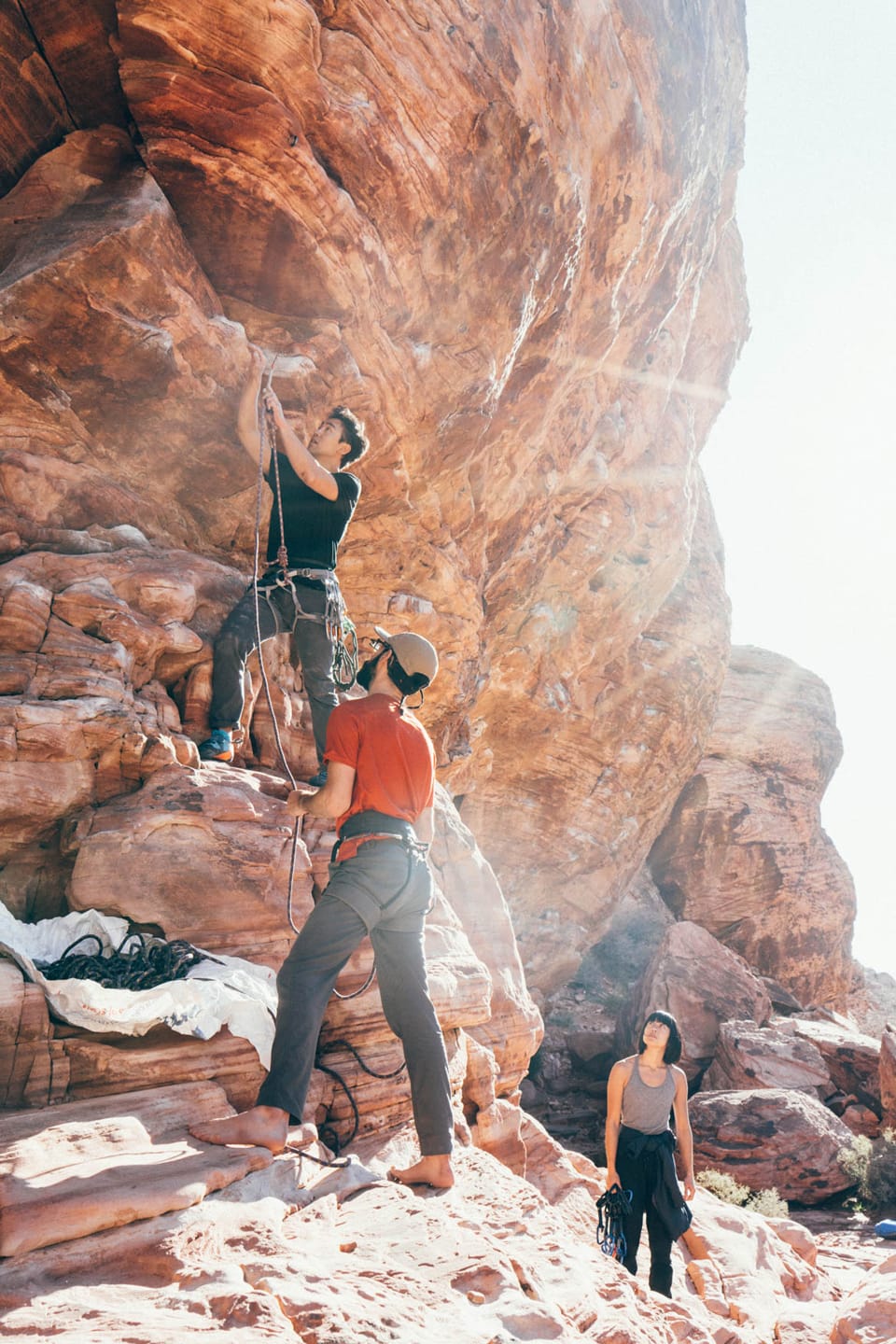 3 climbers look up as one fastens the rope in red rocks