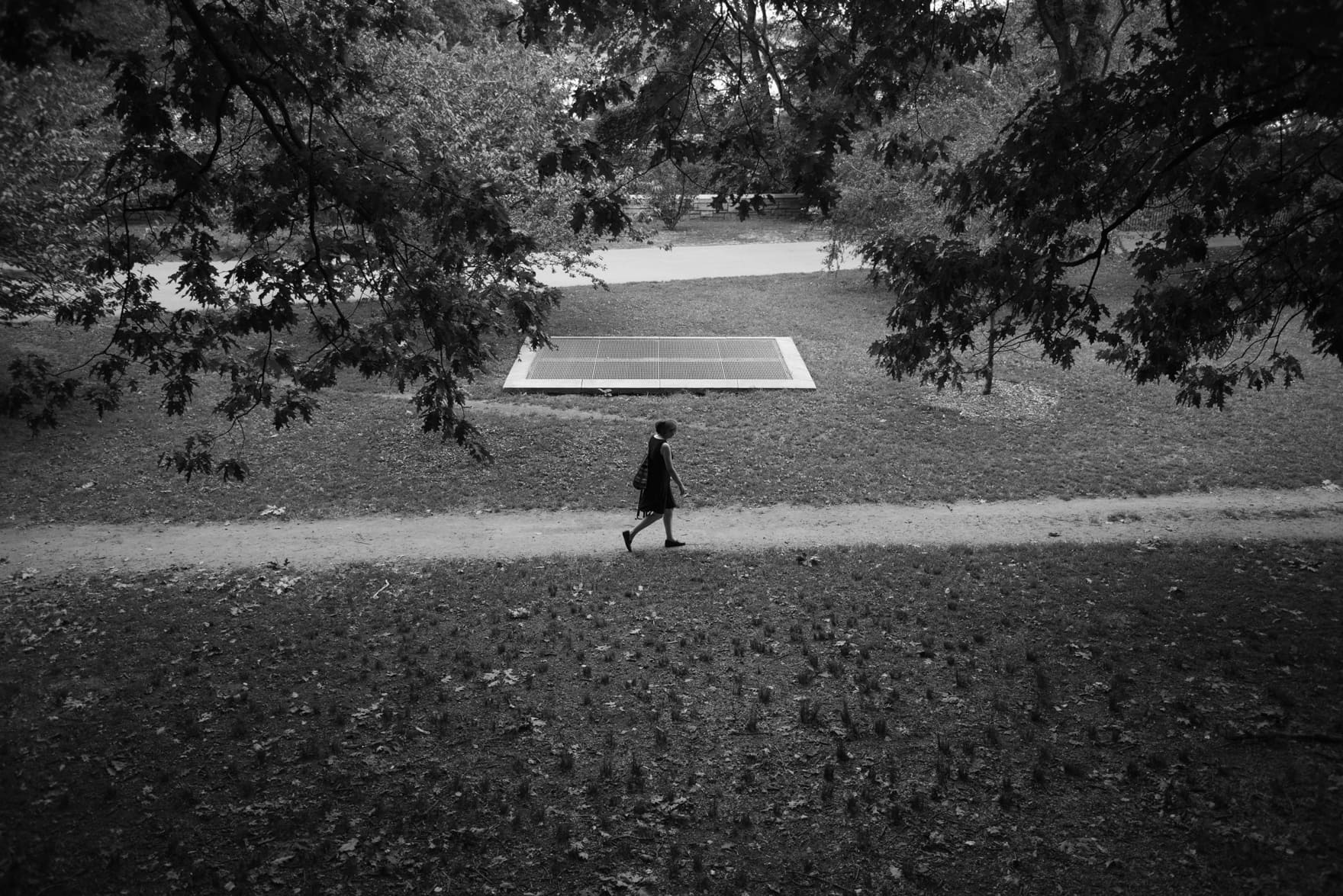 A solo woman walks on a path in Riverside Drive park in the background there is a underground vent